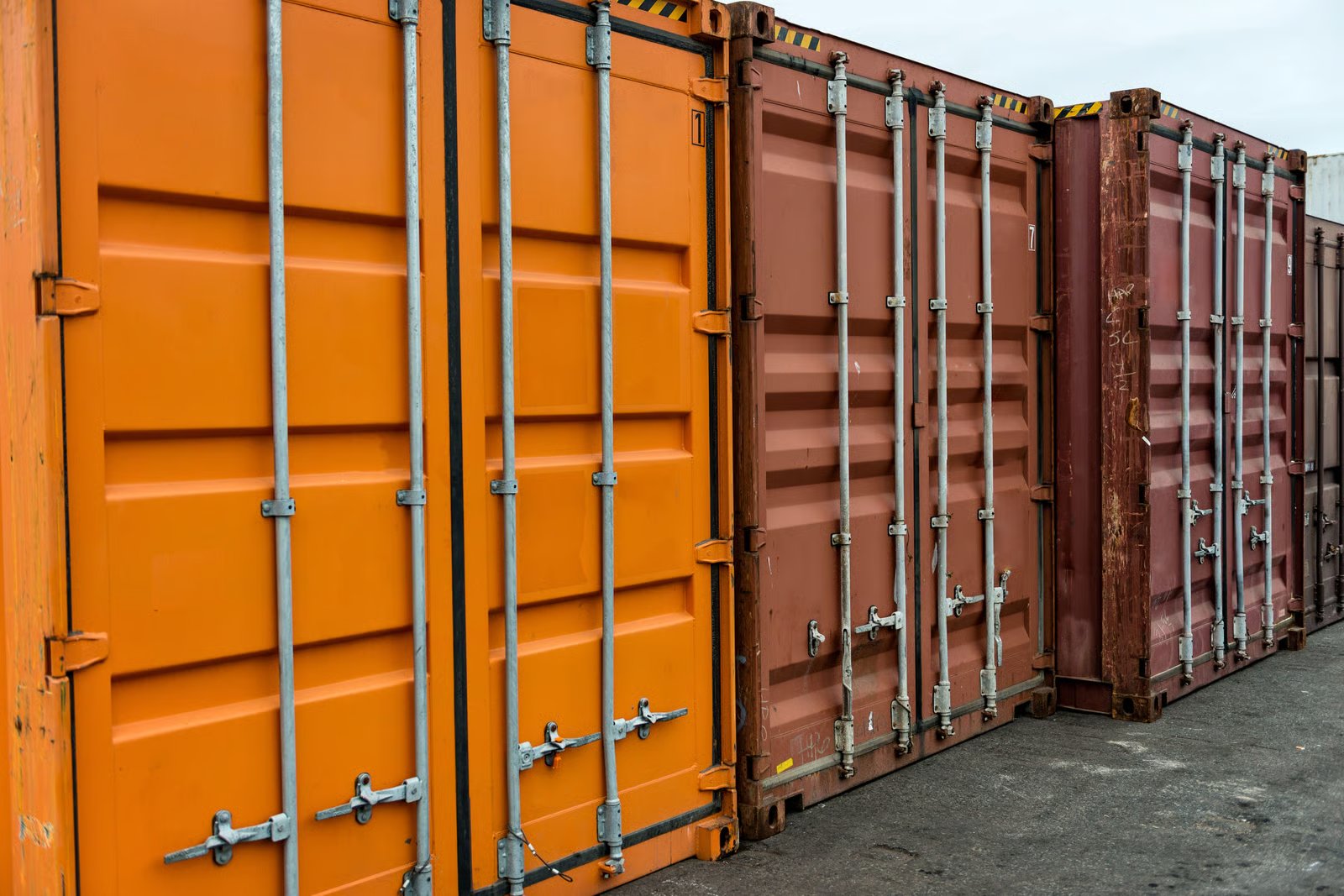 Loading cargo through the narrow end of a standard shipping container is one of the biggest frustrations in logistics. Forklifts struggle with long loads, workers waste time arranging items single-file, and oversized materials simply do not fit through a 7-foot-wide door. The open side container solves these problems by placing full-length doors along the long wall. In this guide, we cover what an open side container is, how the doors work, standard dimensions, real-world applications, pricing, and how it compares to other container types. Infinex can source open side containers for projects across Singapore in both new and used condition. What Is an Open Side Container? An open side container (also called a full-side access container, side-opening container, or side-door container) is a modified intermodal shipping container with bi-fold doors along one or both of its long walls instead of the conventional solid steel panels. While a standard container only has cargo doors on the short 8-foot wall, an open side container opens up the full 20-foot or 40-foot length of its side wall. This gives operators the ability to load, unload, and access cargo from the side rather than being restricted to end-loading only. The bi-fold doors are made from the same corrugated Corten steel as the rest of the container. When closed and sealed, the unit remains wind-tight and water-tight, just like a standard box. Structural integrity is maintained through a reinforced top rail, reinforced corner posts, and carefully engineered hinge systems. Open side containers are built to ISO standards and are compatible with standard container handling equipment. They are available in both 20ft and 40ft lengths, in standard height (8ft 6in) and high cube (9ft 6in) configurations. For a full breakdown of sizing, see our container sizes guide. https://app.envato.com/search/photos/0eb3cb14-fd6f-44ce-b3dc-915d3b4ac1ad?itemType=photos&term=Open+Side+Container&sort=relevance How Open Side Container Doors Work The door system is what sets the open side container apart. Understanding the mechanism, design variants, and opening options will help you choose the right configuration. Bi-Fold Door Mechanism Each door panel is made up of two hinged sections that fold against each other when opened, similar to a closet bi-fold door but built to industrial standards. The doors swing open between 180 and 270 degrees, and when fully opened, the panels fold flat against the adjacent wall or corner post, leaving the entire side opening completely clear. Each panel rides on heavy-duty hinges welded to vertical posts, designed to support 150 to 250 kg per panel while withstanding repeated opening and closing cycles. Doors can be opened individually or all at once, giving you flexibility for partial or full access. Door Configurations Full open-side (no centre post): Two large bi-fold assemblies meet in the middle. When opened, the entire wall is clear with no vertical obstruction. Best for very long or wide items. One-post/two-door: A single vertical centre post divides the side into two openings, each with its own bi-fold assembly. Adds structural rigidity while providing generous access. Four-door/three-post: Three vertical posts create four equal door sections. Highest structural strength, commonly chosen when stacking is required. Most open side containers also retain the standard end doors, giving you dual-access capability. Weatherproofing and Security Despite having an entire wall that opens, open side containers are engineered to be fully weather-tight when closed: Rubber gaskets: Continuous seals along every door edge, post junction, and threshold create a water-tight barrier Multi-point locking: Cam-action lock rods engage at the top, bottom, and middle of each door frame, with high-security padlock hasps Drainage channels: Door tracks and bottom rails direct water away from the interior Wind rating: Closed and locked units meet the same wind resistance standards as conventional containers, typically rated for sustained winds up to 150 km/h https://app.envato.com/search/photos/3e91e6b3-9ae2-4f67-a910-615e4992888f?itemType=photos&term=Open+Side+Container&sort=relevance Open Side Container Dimensions and Specifications Below are the standard dimensions for the most common open side container sizes. Exact measurements may vary slightly between manufacturers. 20ft Open Side Container (Standard and High Cube) Specification 20ft Standard 20ft High Cube External Dimensions (L x W x H) 6,058 x 2,438 x 2,591 mm 6,058 x 2,438 x 2,896 mm Internal Dimensions (L x W x H) 5,898 x 2,350 x 2,390 mm 5,898 x 2,350 x 2,690 mm Side Door Opening (W x H) 5,758 x 2,280 mm 5,758 x 2,585 mm End Door Opening (W x H) 2,340 x 2,280 mm 2,340 x 2,585 mm Tare Weight 2,550 to 2,800 kg 2,750 to 3,050 kg Maximum Payload 21,500 to 24,000 kg 21,000 to 24,000 kg Cubic Capacity 33.0 to 33.2 cbm 37.2 to 37.5 cbm 40ft Open Side Container (Standard and High Cube) Specification 40ft Standard 40ft High Cube External Dimensions (L x W x H) 12,192 x 2,438 x 2,591 mm 12,192 x 2,438 x 2,896 mm Internal Dimensions (L x W x H) 12,032 x 2,350 x 2,390 mm 12,032 x 2,350 x 2,690 mm Side Door Opening (W x H) 11,832 x 2,280 mm 11,832 x 2,585 mm End Door Opening (W x H) 2,340 x 2,280 mm 2,340 x 2,585 mm Tare Weight 4,200 to 4,800 kg 4,500 to 5,200 kg Maximum Payload 26,000 to 28,000 kg 26,000 to 28,500 kg Cubic Capacity 67.3 to 67.7 cbm 75.8 to 76.3 cbm Construction and Materials Open side containers use the same industrial-grade materials as standard shipping containers, with additional reinforcement to compensate for the opening side wall. Corten steel (weathering steel): Walls, roof, floor frame, and door panels are fabricated from Corten steel, which forms a protective rust layer that shields the underlying metal from corrosion. Ideal for containers exposed to rain, salt spray, and tropical humidity. Reinforced frame: The top side rail, corner posts, and bottom side rail are all reinforced with heavier gauge steel sections to maintain load-bearing capacity after removing the solid wall. Marine-grade plywood flooring: 28 mm thick, treated with insecticide and fungicide, rated to support forklift traffic and heavy point loads. Forklift pockets: Standard ISO-spaced pockets built into the base for lifting and repositioning. Heavy-duty hardware: Forged steel hinges designed for tens of thousands of cycles. All lock rods, handles, and cam keepers are zinc-plated or galvanised. Multi-layer coating: Zinc-rich primer, intermediate epoxy coat, and marine-grade polyurethane topcoat for long-term corrosion protection. Advantages of Open Side Containers Full forklift access from the side. A forklift can approach perpendicular to the container and place pallets anywhere inside without driving through a narrow 8-foot corridor. Faster loading and unloading. Multiple workers or machines can operate along the open side simultaneously. Side-loading can reduce handling time by 30% to 50% compared to end-loading. Oversized cargo capability. Items wider than the 7 ft 8 in end door can be loaded through the side opening, which stretches up to 38 ft 10 in on a 40ft unit. Reduced cargo damage. Items can be placed directly into position rather than being dragged or tilted through a narrow door. Easy access to all cargo. Every item is immediately reachable from the side, making inventory management and partial unloading far more practical. Outstanding conversion potential. The full-length opening is perfect for large windows, folding walls, serving hatches, or roll-up shutters, making these containers ideal for customised solutions. Storefront and display capability. When opened, the container creates a natural covered shopfront. The roof provides shade and rain protection while the full interior is visible. Weather-tight when closed. Rubber gaskets and multi-point locks ensure the container is fully sealed, meeting the same standards as conventional containers. Strong resale value. Limited supply and strong demand mean open side containers hold their value well. https://app.envato.com/search/photos/1325f9a0-18cb-4bc5-bef3-f56045e3edf1?itemType=photos&term=Open+Side+Container&sort=relevance Disadvantages of Open Side Containers Higher purchase cost. Open side containers cost approximately 1.5 to 2 times more than a comparable standard container due to complex door engineering and reinforced framing. Heavier tare weight. The reinforced frame and bi-fold doors add 200 to 500 kg, slightly reducing maximum payload capacity. Limited availability. These are a specialty product with limited production volumes. Lead times for new orders are typically 8 to 14 weeks. Used open side containers are particularly scarce. Lateral clearance required. The bi-fold doors need 600 to 800 mm of clearance to swing open, which can be a constraint in tight spaces. Reduced stacking capacity. Most are rated for 3 to 5 high stacking when empty, compared to 6 to 9 for standard containers. Always check the CSC plate. Door maintenance. Hinges, lock rods, and gaskets require periodic lubrication and inspection, especially in coastal or tropical environments. Open Side Container Uses and Applications Construction sites. Side-loading allows teams to store and access timber, steel beams, pipes, scaffolding, and heavy equipment without tight end-door manoeuvring. Multiple trades can access different sections simultaneously. Browse our range of products suitable for construction. Warehousing and distribution. Open side containers serve as flexible overflow storage during peak seasons. Side access makes pick-and-pack operations faster and enables proper first-in, first-out inventory rotation. Retail pop-up shops and events. When opened, the container transforms into a sheltered, branded retail or food-service space. Lockable when closed for overnight security. Ideal for markets, festivals, product launches, and trade shows. Agriculture. The side access is useful for loading large hay bales with a tractor-mounted loader or storing equipment too wide for standard doors. Military and emergency services. Side-loading enables rapid deployment and distribution of supplies, equipment, and field infrastructure in time-sensitive operations. Modular conversions. The pre-engineered full-length opening saves significant fabrication costs compared to cutting and reinforcing a standard container wall. Architects use these for offices, studios, cafes, garages, and modular homes. Explore Infinex customised container solutions for conversion options. Open Side Container vs Other Container Types Feature Open Side Standard Double-Door (Tunnel) Curtain-Sided Open Top Side wall access Full-length bi-fold doors Fixed steel panel Fixed steel panel PVC/canvas curtains Fixed steel panel End doors Standard double doors Standard double doors Double doors on both ends Standard double doors Standard double doors Loading direction Side and end End only Both ends Side and end Top and end Max opening width (40ft) Up to 38 ft 10 in 7 ft 8 in 7 ft 8 in (each end) Full side length 7 ft 8 in Security level High (steel doors, multi-point locks) High High Low (curtains can be cut) Medium (tarpaulin roof) Weather tightness Full (gaskets and locks) Full Full Partial Partial Stacking capacity 3 to 5 high 6 to 9 high 5 to 7 high 2 to 3 high 4 to 6 high Tare weight (20ft) 2,550 to 2,800 kg 2,200 to 2,350 kg 2,400 to 2,600 kg 2,300 to 2,500 kg 2,300 to 2,500 kg Price (20ft new) $6,500 to $9,500 $3,000 to $5,000 $4,000 to $6,500 $5,000 to $7,500 $4,500 to $7,000 Availability Limited Widely available Moderate Limited Moderate Best for Side access, oversized cargo, conversions General cargo, shipping Drive-through access Fast roadside loading Top-loading with crane Open Side Container Pricing Open side container prices depend on size, condition, door configuration, and market availability. Below is a guide to current pricing in the Singapore and Southeast Asian market. Condition 20ft Price (USD) 40ft Price (USD) New (one-trip) $6,500 to $9,500 $9,500 to $15,000 Refurbished $5,000 to $7,000 $7,500 to $11,000 Used (good condition) $4,000 to $6,000 $6,000 to $9,000 40ft high cube open side containers sit at the upper end of these ranges due to additional material and higher demand. Used open side containers are significantly harder to find than used standard containers. When available, check the condition of doors, gaskets, hinges, and locking mechanisms carefully, as these components experience the most wear. Check our used container inventory for current availability. Why Open Side Containers Cost More The higher price reflects complex bi-fold door engineering, heavier structural reinforcement, specialised hardware components, lower production volumes, and additional quality control testing for door alignment and gasket sealing. For container accessories such as additional locks, shelving, or lighting to complement your open side container, visit our accessories page. https://app.envato.com/search/photos/5a67a99c-d148-4bdd-a4c8-2672d08942e6?itemType=photos&term=Open+Side+Container&sort=relevance Frequently Asked Questions 1. What is an open side container used for? An open side container is used for any application that benefits from full-length side access, including construction site storage, warehousing, retail pop-up shops, agricultural storage, military logistics, and modular building conversions. 2. Can an open side container be shipped by sea? Yes. Open side containers are built to ISO standards and can be shipped on container vessels, trailer chassis, and rail. Ensure the doors are properly secured and sealed according to carrier requirements. 3. Are open side containers waterproof? Yes. When all doors are closed and locked, the rubber gaskets and multi-point locking system create a weather-tight seal meeting the same standards as conventional shipping containers. 4. Can I stack open side containers? Yes, but with reduced capacity. Most are rated for 3 to 5 high stacking when empty. Always check the CSC plate on the specific unit for its approved stacking weight. 5. Can the side doors be removed? Yes. The bi-fold doors are mounted on bolt-on hinges and can be removed if a permanent full-side opening is desired. This is commonly done for conversion projects. 6. Do open side containers have end doors too? Most open side containers retain the standard double doors on the short end wall, giving you dual-access capability. Side-only models (no end doors) are less common. 7. Can I convert an open side container into a shop or office? Absolutely. Open side containers are among the most popular choices for container conversions. The full-length opening provides a ready-made shopfront, display area, or large window opening. Infinex offers customised container solutions for fit-outs of all types. 8. How quickly can I get an open side container in Singapore? New one-trip containers typically have lead times of 8 to 14 weeks. In-stock units can often be delivered within 3 to 7 business days. Contact Infinex for availability and pricing through our services page or contact us directly to discuss your requirements.